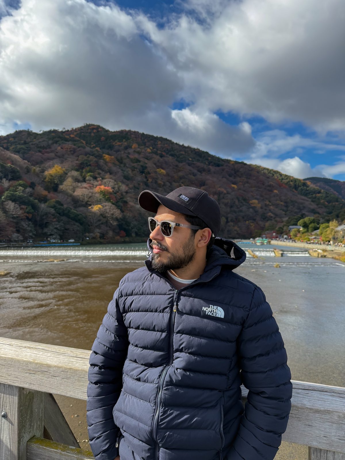 Faiq on the wooden bridge at Arashiyama with autumn mountains behind